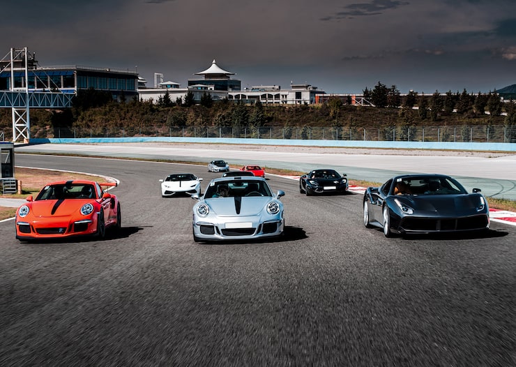 Group of exotic sports cars, including Porsche and Ferrari models, parked together on a racetrack